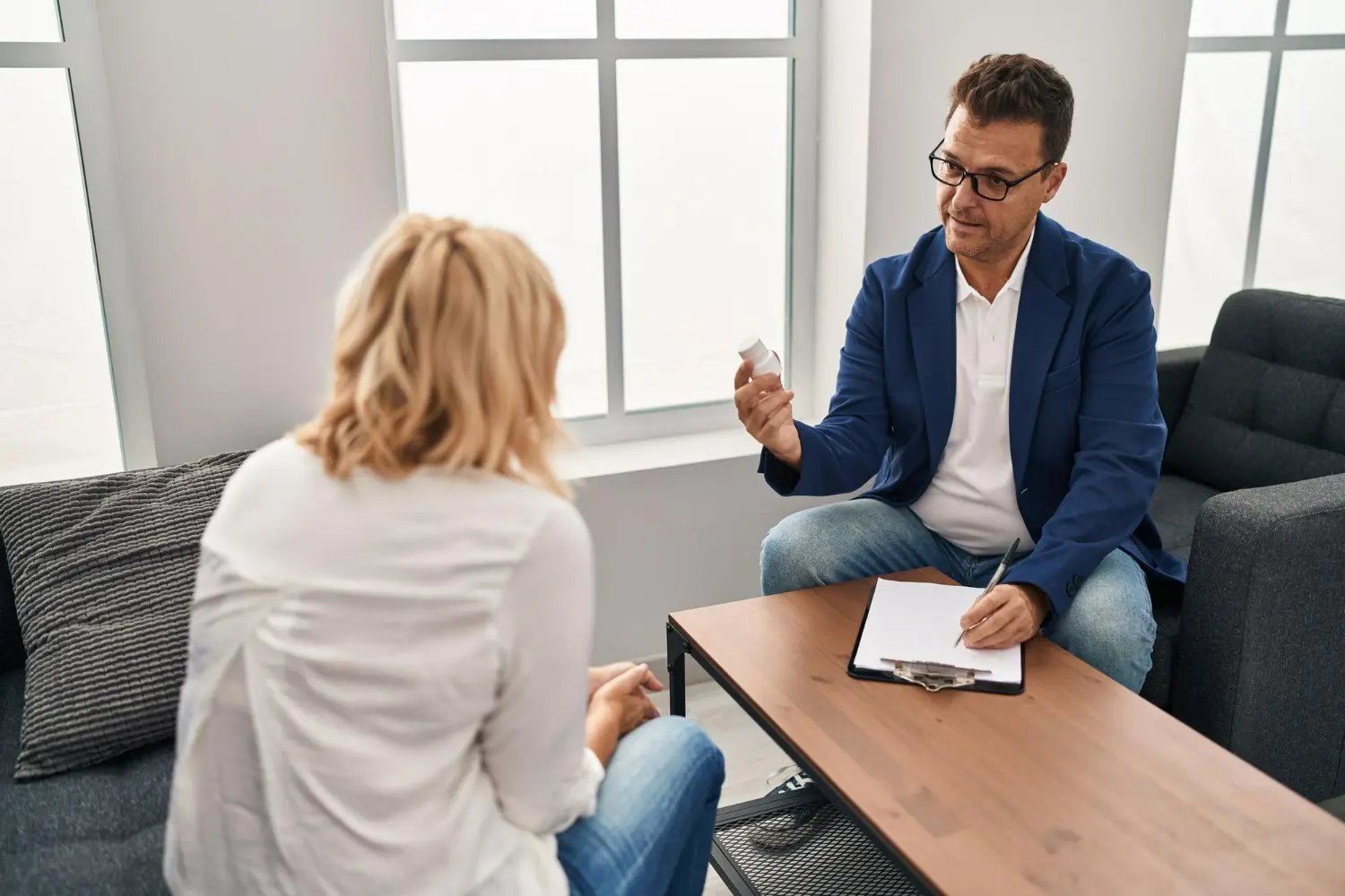 Therapist discussing treatment options with a client, showcasing a bottle of medication in a modern counseling setting.