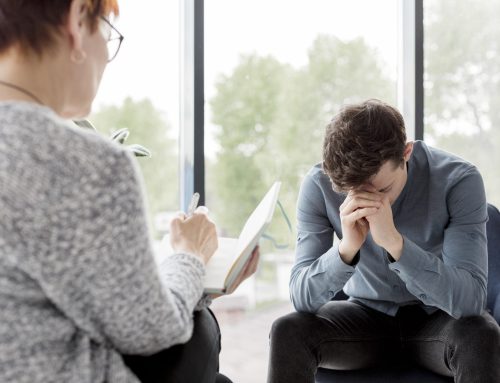 Man in therapy session with head down, expressing distress, while therapist takes notes.