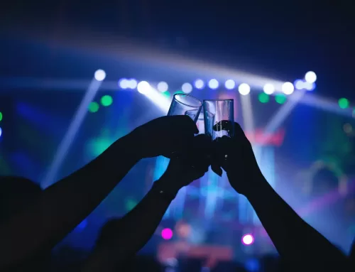 Hands toasting with drinks in a vibrant nightlife setting, highlighting social triggers related to substance use and addiction recovery.